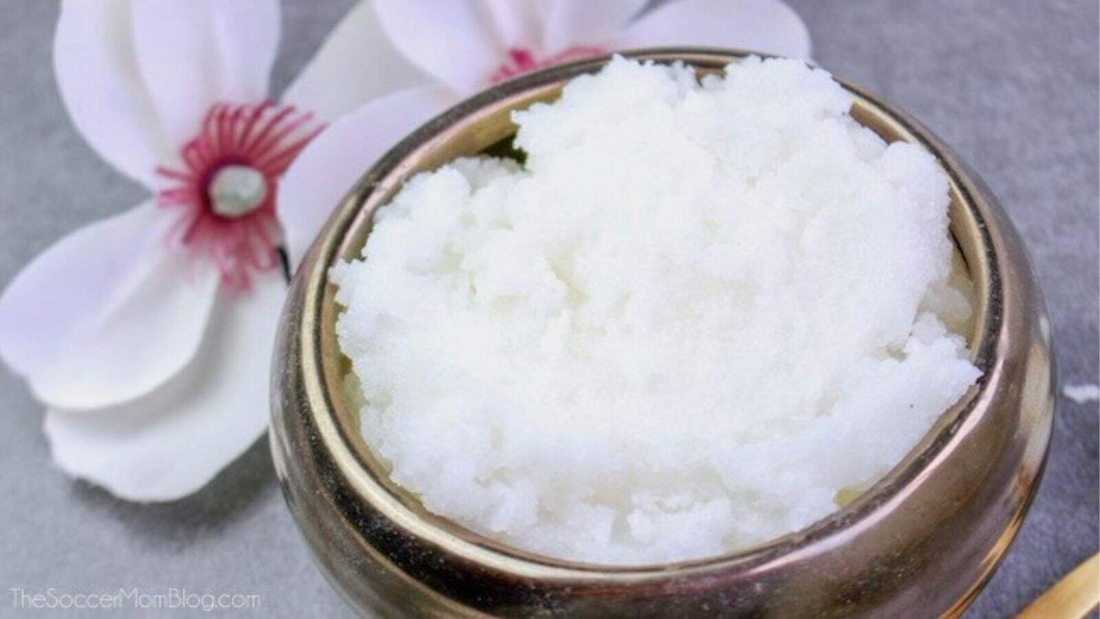 A bowl filled with a white, fluffy substance sits next to two white flowers with pink centers on a gray surface.