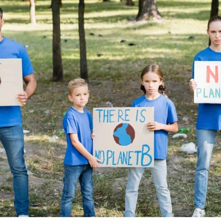 Four people, two adults and two children, stand outdoors holding signs with environmental messages such as "Save," "There is no planet B," and "No Planet B.