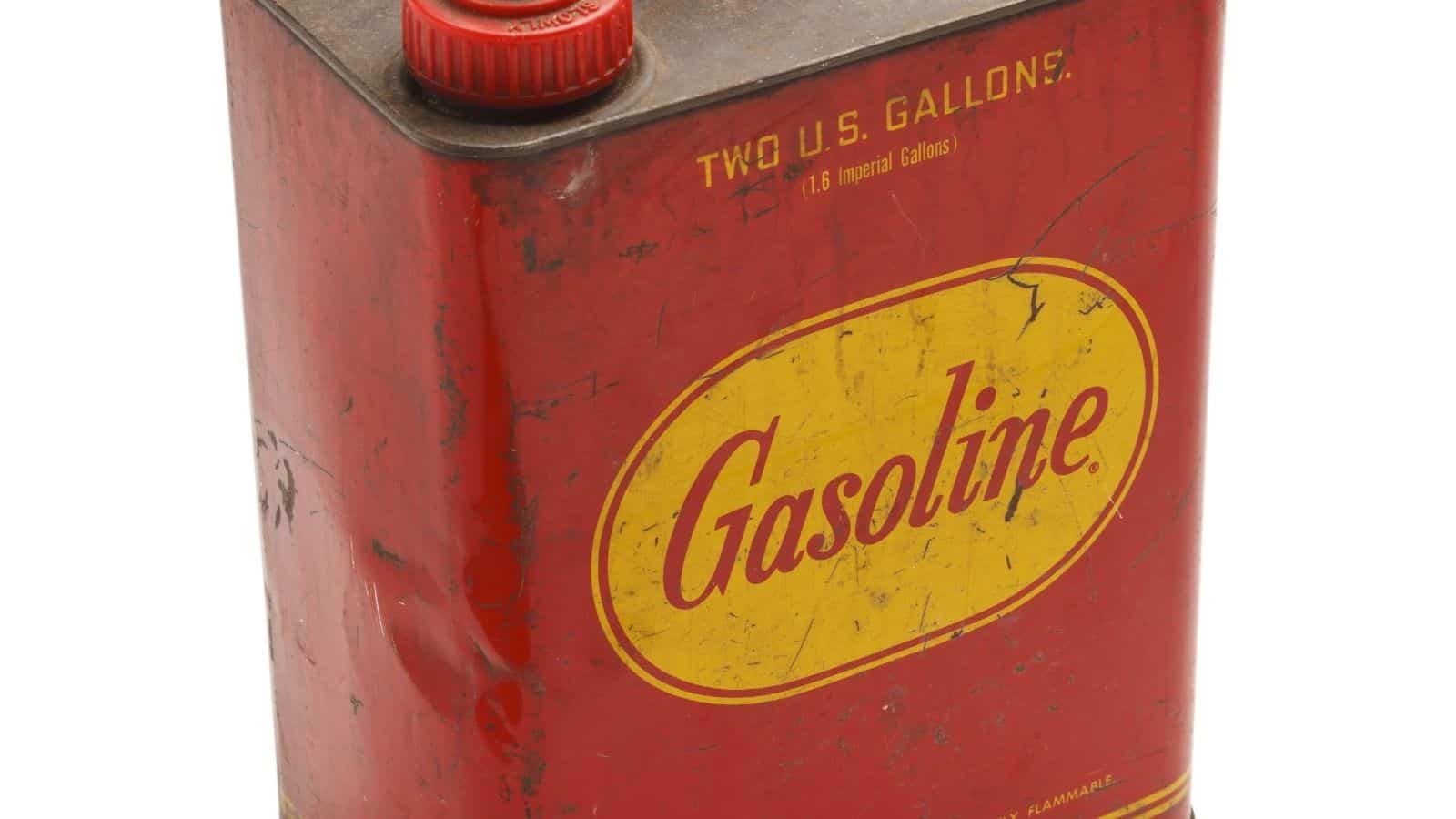 A vintage red metal gasoline can with a yellow label reading "Gasoline" and a red screw cap, marked "TWO U.S. GALLONS" at the top.