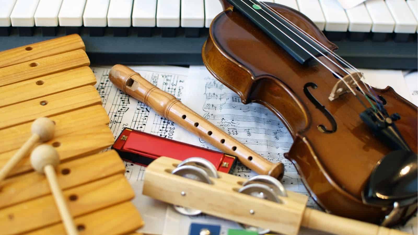 A violin, recorder, harmonica, xylophone, and rhythm sticks are placed on sheet music in front of a keyboard.