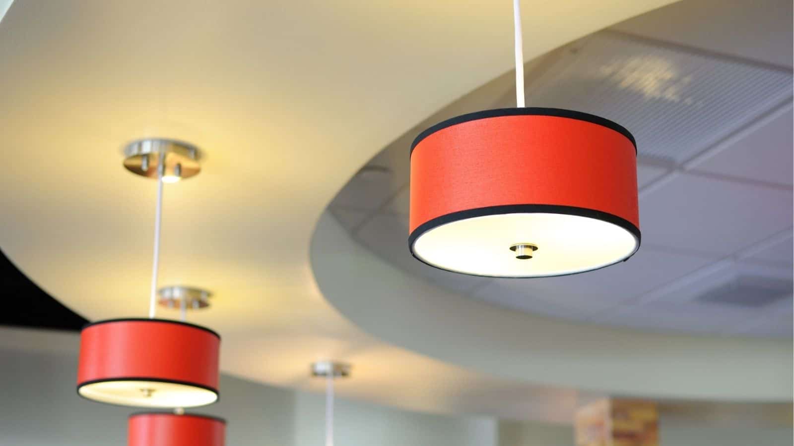 Three ceiling lights with red cylindrical lampshades hang from a white curved ceiling structure in a modern interior space.