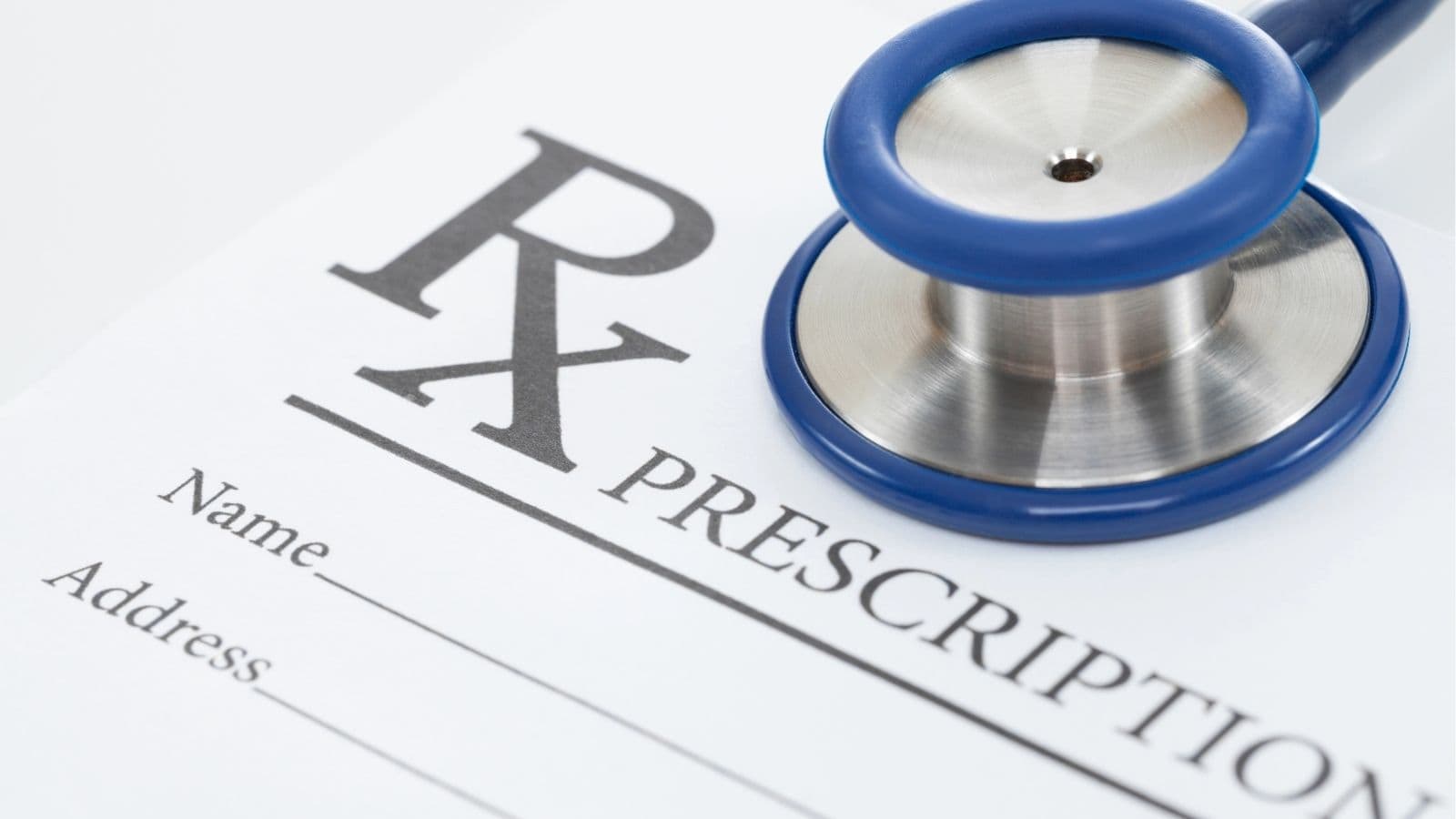 A stethoscope rests on a blank prescription form labeled "Rx," with spaces for name and address.