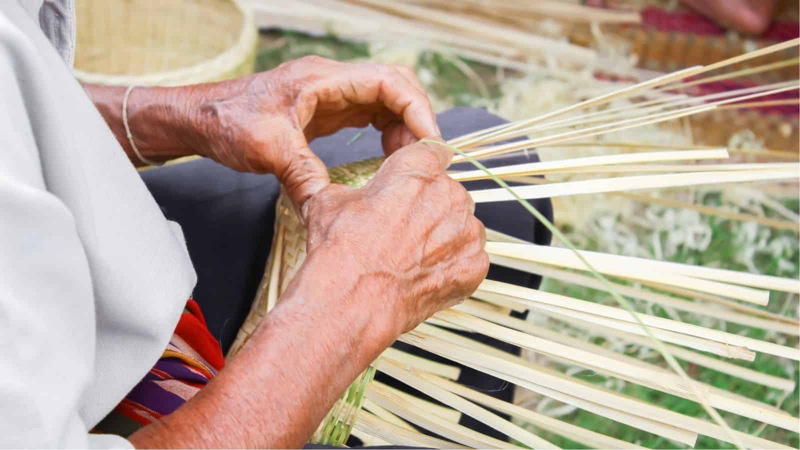 Close-up of a person weaving thin strips of bamboo or reed to make a basket, showing skilled hands in the process of traditional basketry.