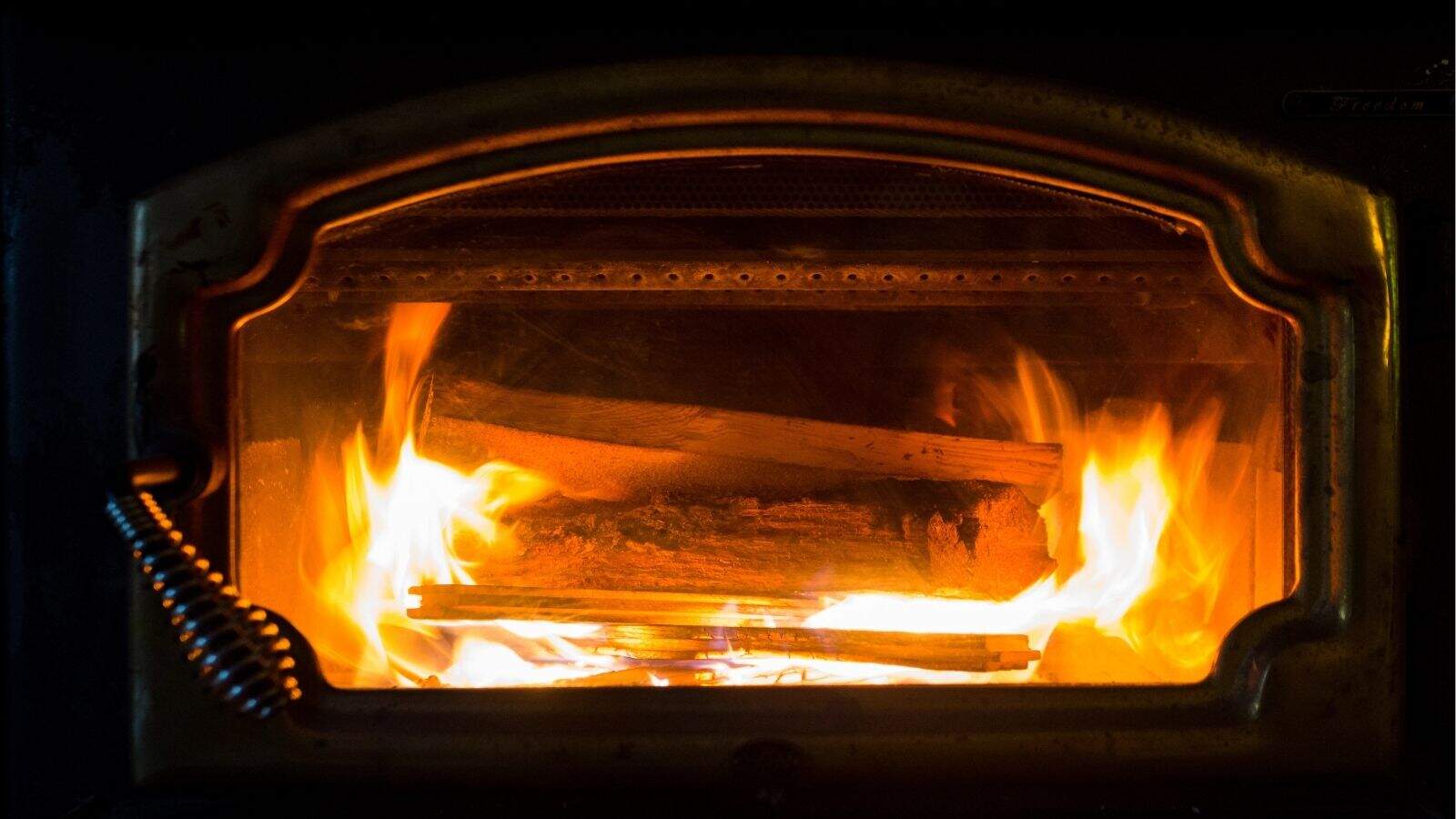 A close-up view of burning logs inside a wood stove with visible flames through the glass door.