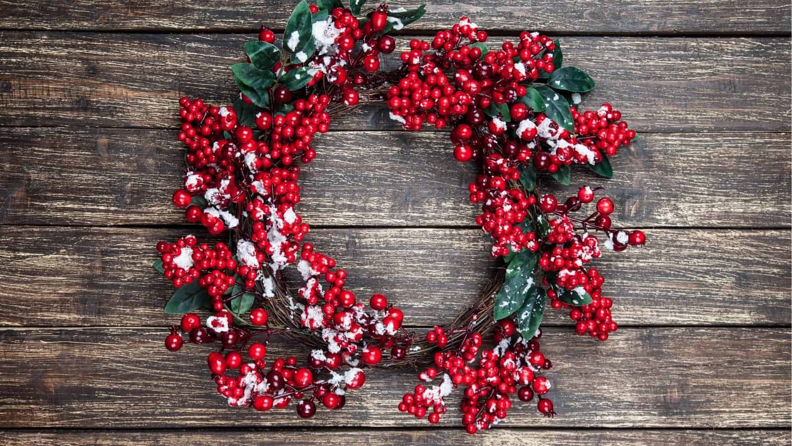 A wreath made of red berries and green leaves with artificial snow, placed on a rustic wooden surface.