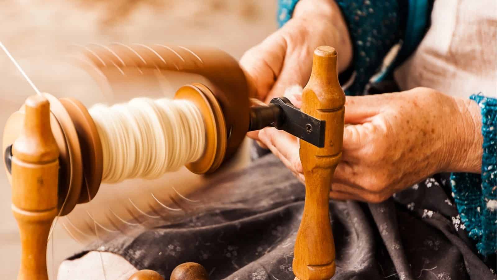 Close-up of hands spinning wool using a traditional spinning wheel, with motion blur showing the wheel turning.