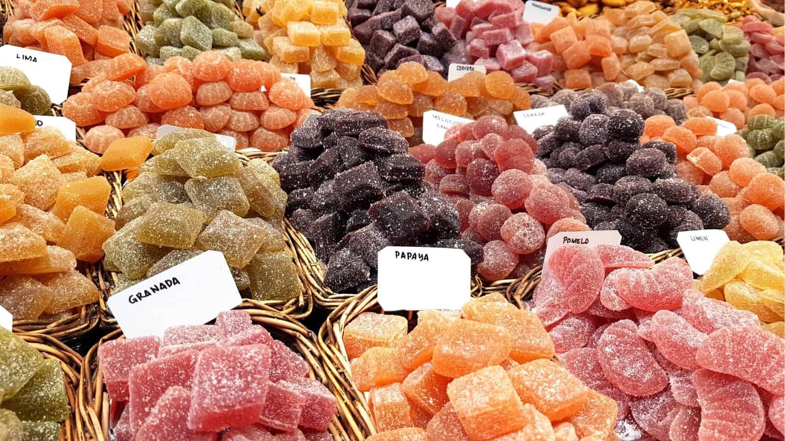 Assorted baskets of colorful fruit jelly candies with labels, arranged in rows at a market or store.