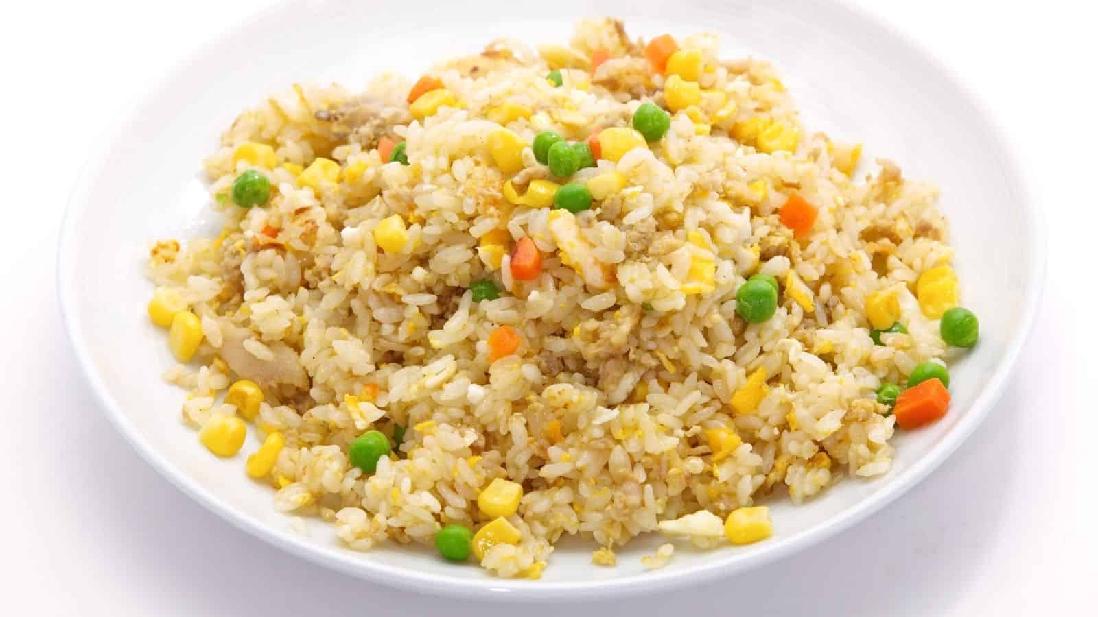 A plate of fried rice with peas, corn, carrots, and small pieces of egg and meat on a white background.