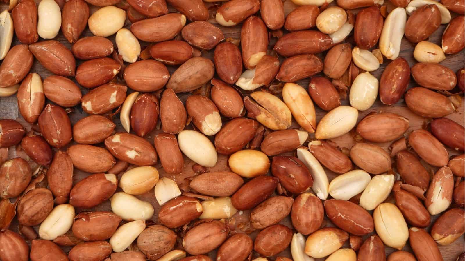 A close-up view of shelled, raw peanuts, some with skins partially removed, spread out in a scattered arrangement.