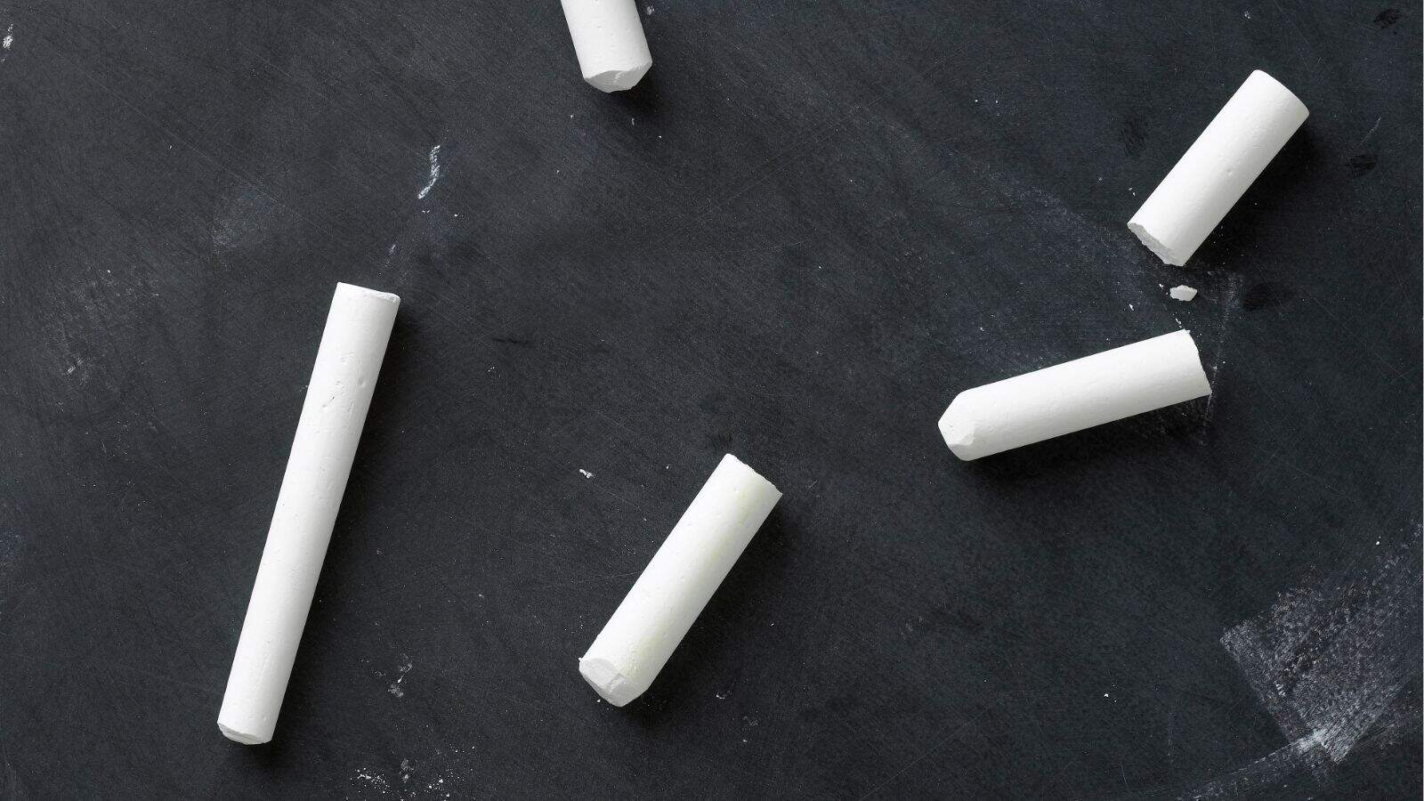 Five pieces of white chalk, some broken, are scattered on a dark chalkboard surface.
