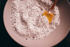 A ceramic bowl containing a dry mixture of flour and herbs, with a yellow spatula resting inside.