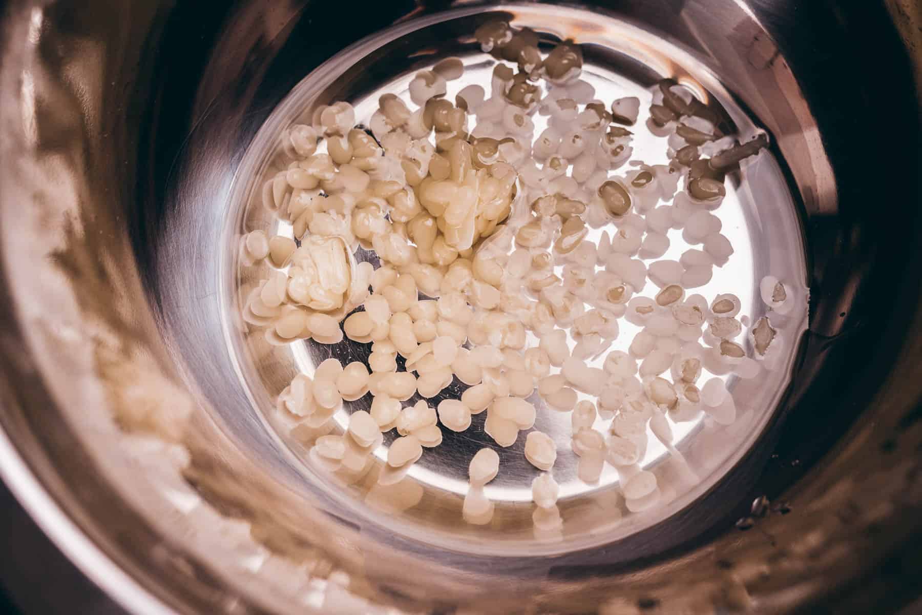 White wax pellets and a small amount of solid butter are in the bottom of a shiny metal mixing bowl.