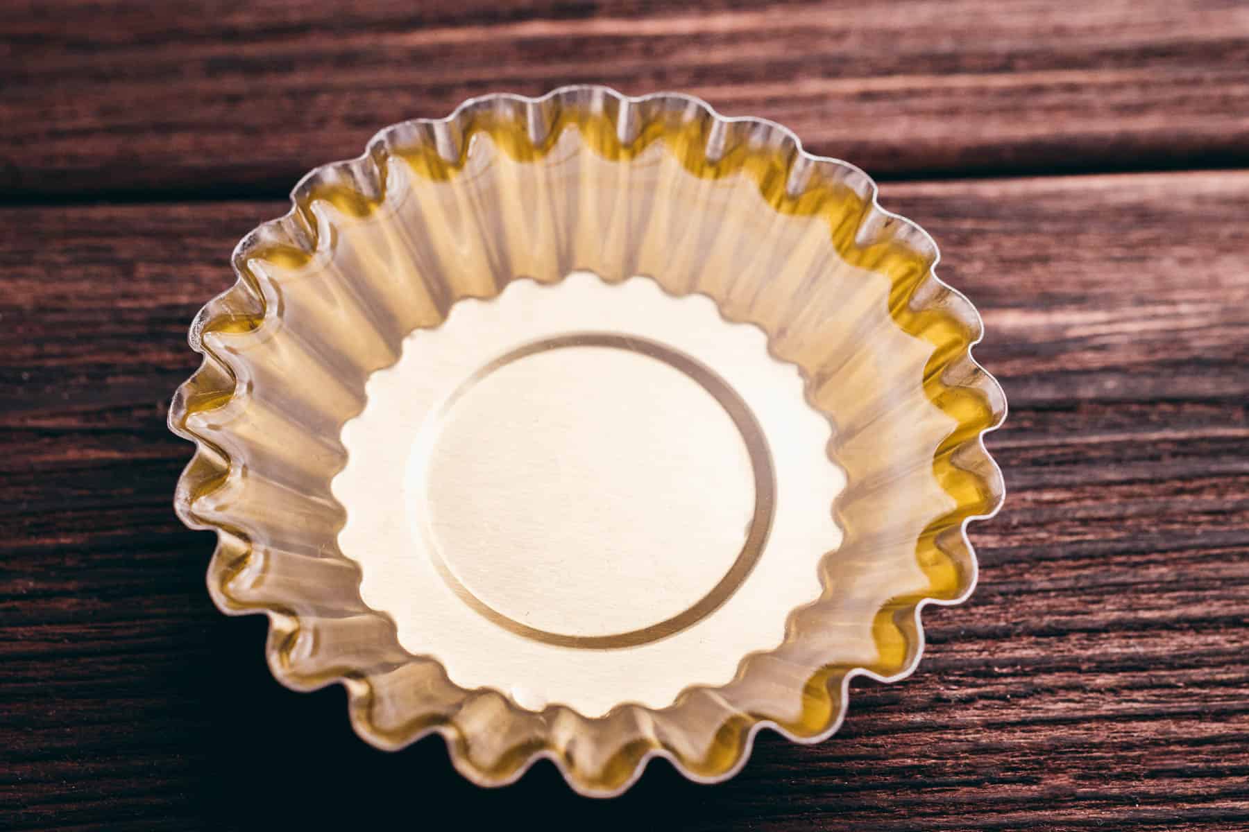 A single empty golden cupcake liner sits on a dark wooden surface, viewed from above.