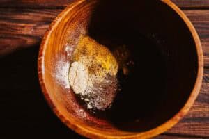 Wooden bowl containing piles of various dry spices and powders for a fire cider electuary.