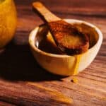 A wooden spoon rests in a small wooden bowl filled with honey, often used to create a fire cider electuary.
