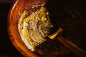 A yellow spatula stirs a fire cider electuary mixture of flour and spices in a wooden bowl.