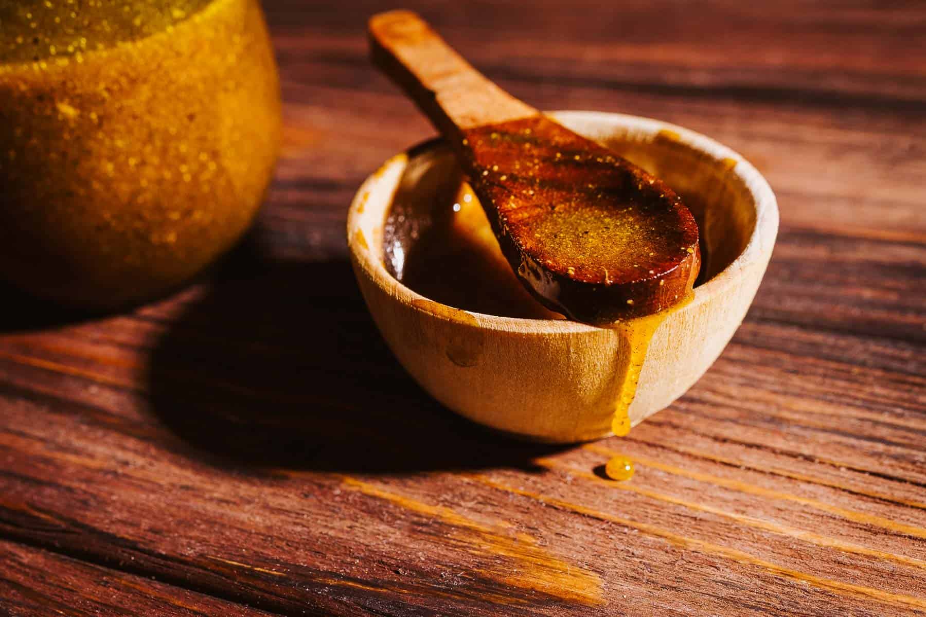 A wooden spoon rests in a small wooden bowl filled with amber-colored fire cider.