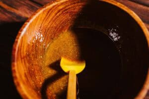 A wooden bowl containing a dark, oily fire cider electuary being stirred with a yellow silicone spatula.