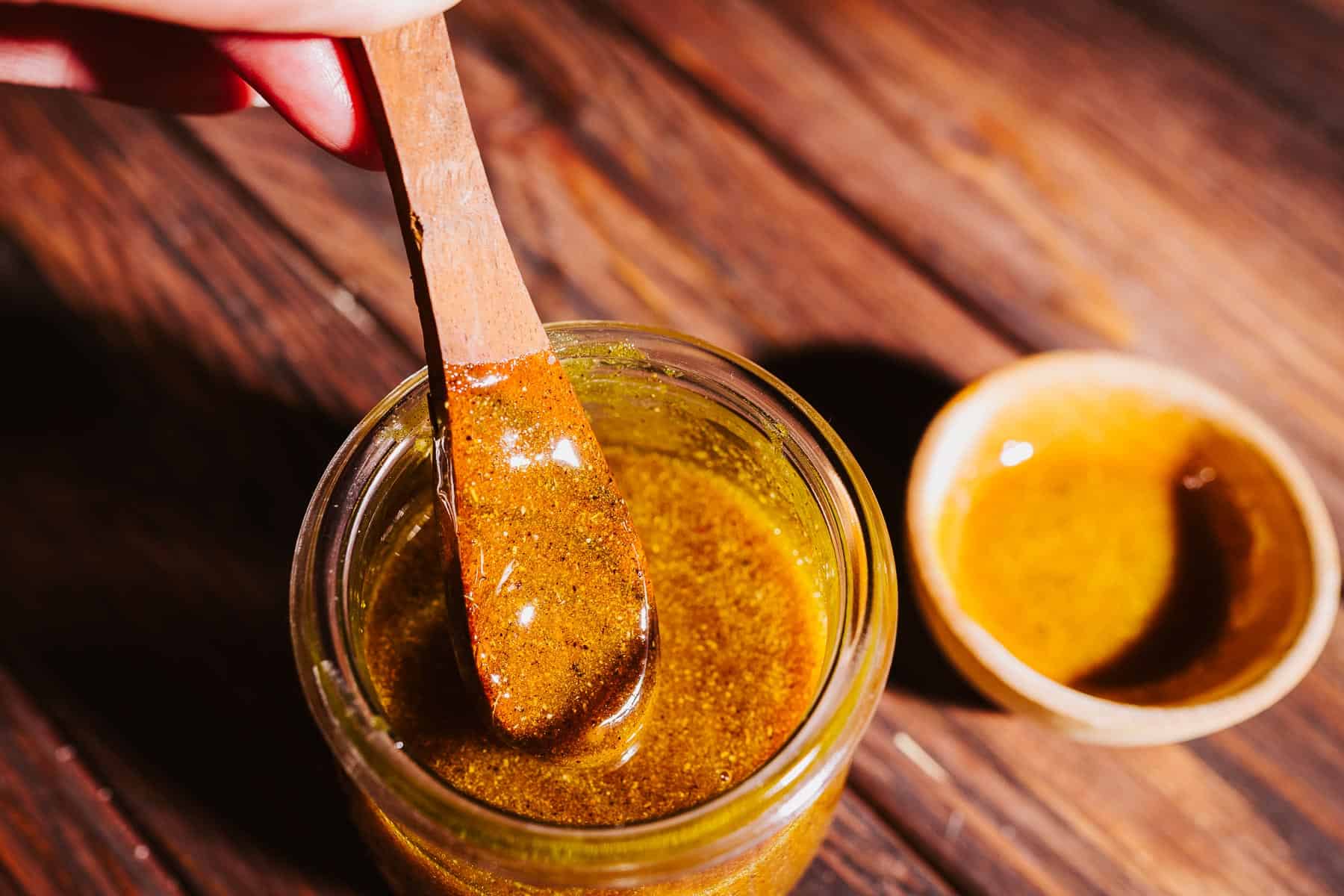 A wooden spoon lifting spiced fire cider honey from a glass jar.