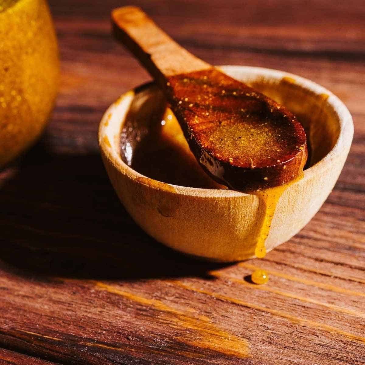A wooden spoon rests in a small wooden bowl filled with honey, often used to create a fire cider electuary.