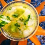A glass of citrus drink with ice, lime wedges, and mint leaves, viewed from above.