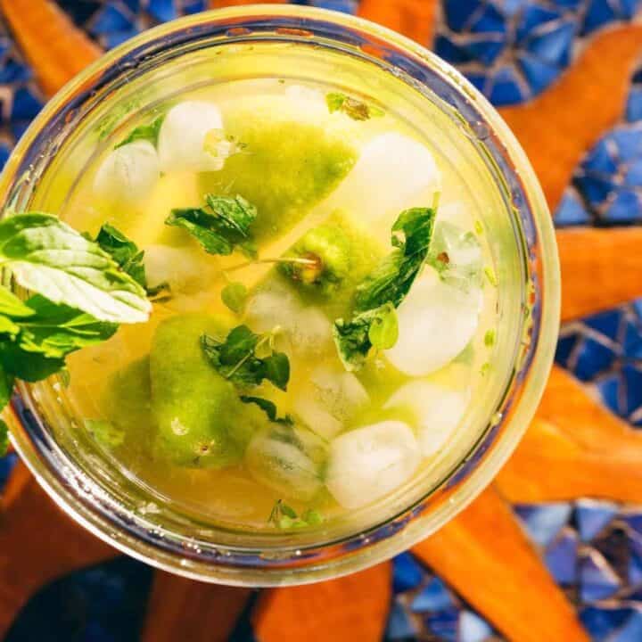 A glass of citrus drink with ice, lime wedges, and mint leaves, viewed from above.