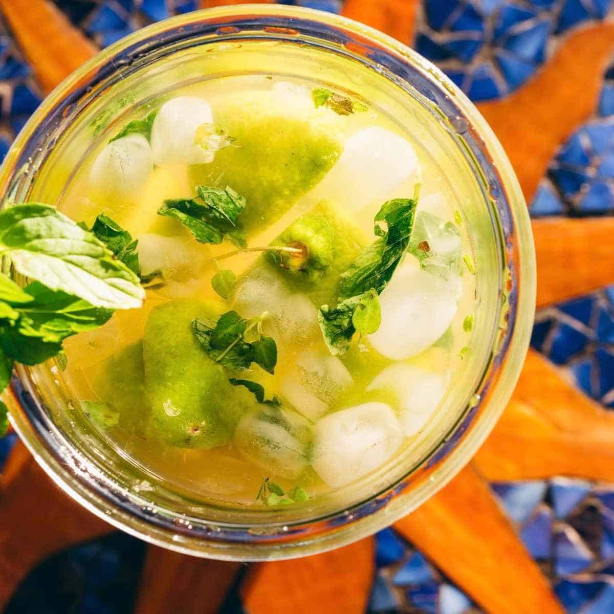A glass of citrus drink with ice, lime wedges, and mint leaves, viewed from above.