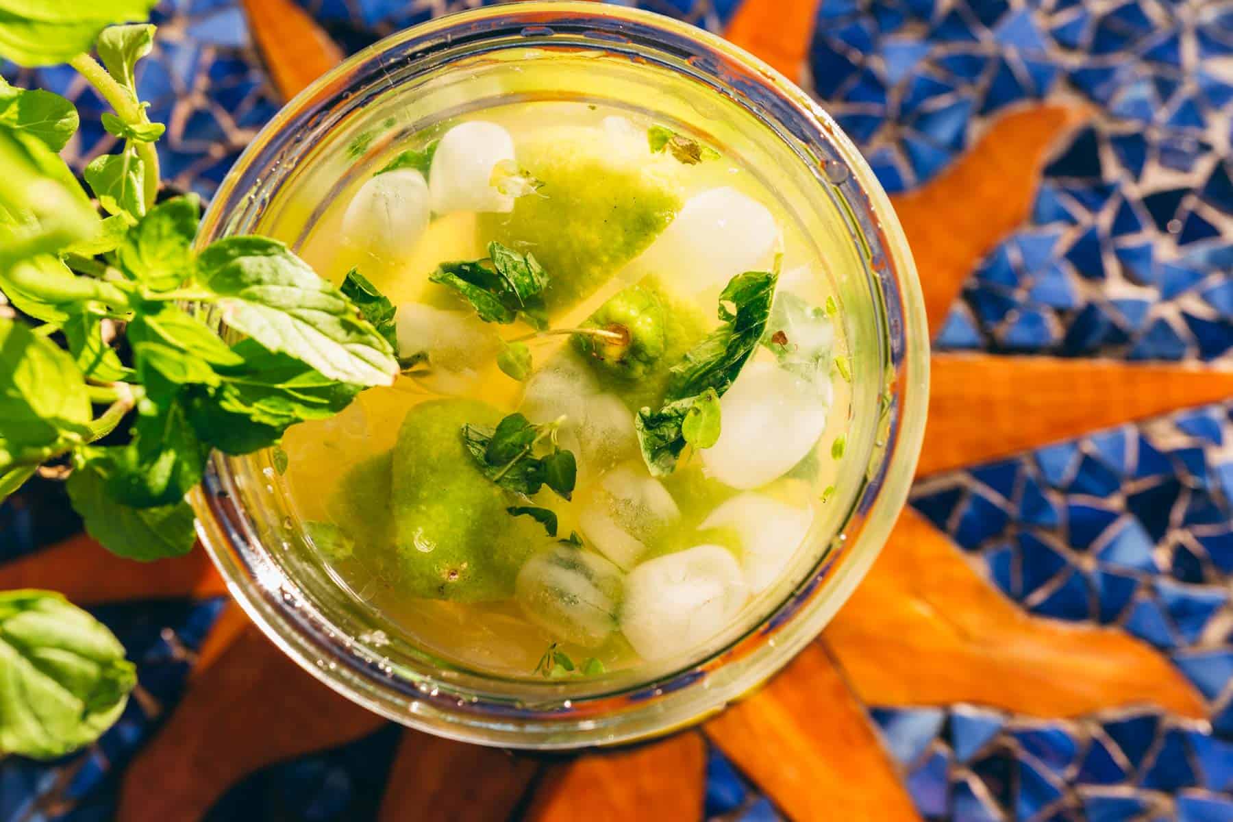 A top-down view of a glass containing a lime and mint drink with ice, garnished with fresh mint leaves.