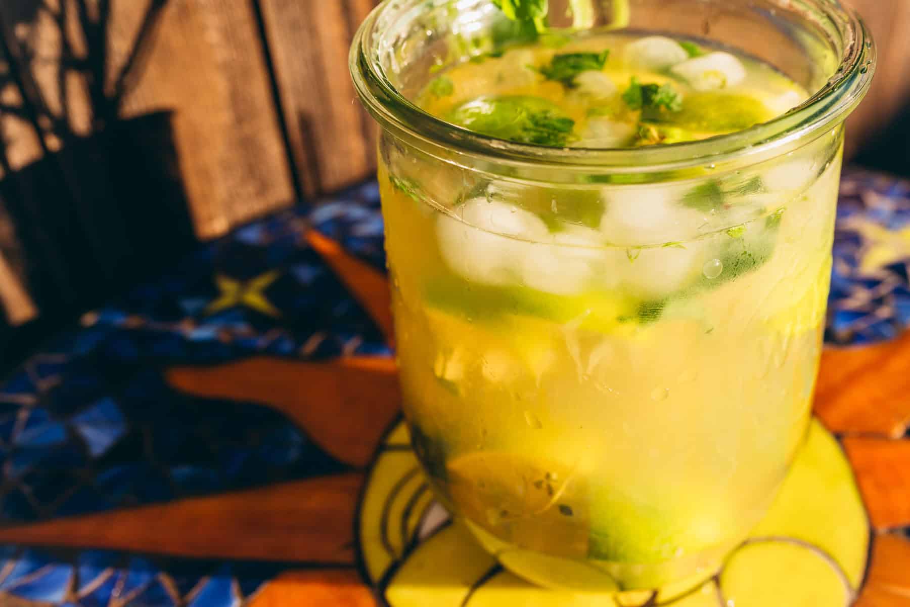 A glass of iced limeade with lime slices and mint leaves on a tiled table.