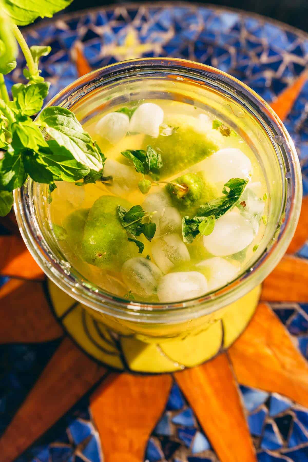 A glass of limeade with ice, lime wedges, and fresh mint leaves, viewed from above.