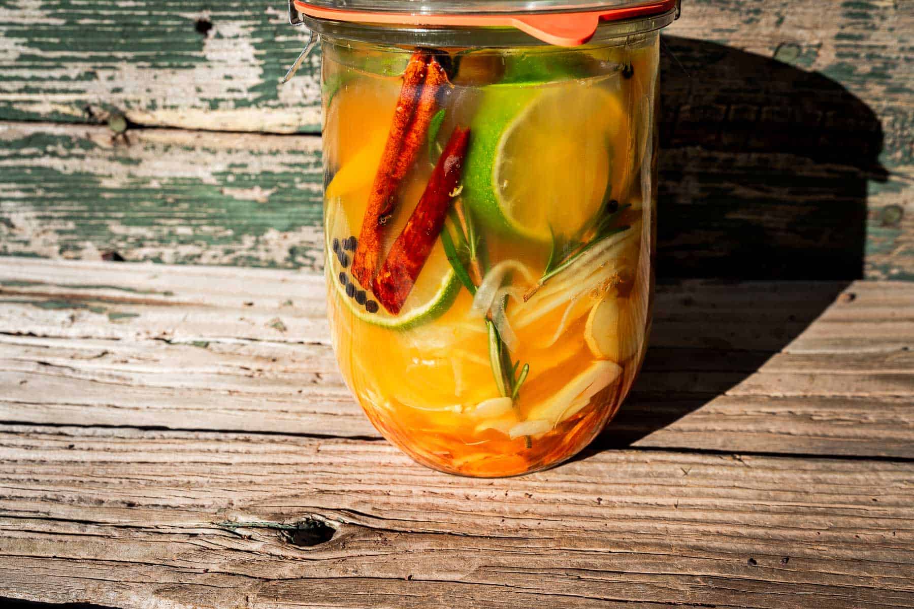 Glass jar filled with a fire cider infusion of citrus slices, cinnamon sticks, herbs, and spices.