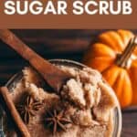 A glass jar of homemade pumpkin spice sugar scrub accompanied by a wooden spoon, cinnamon sticks, and star anise.